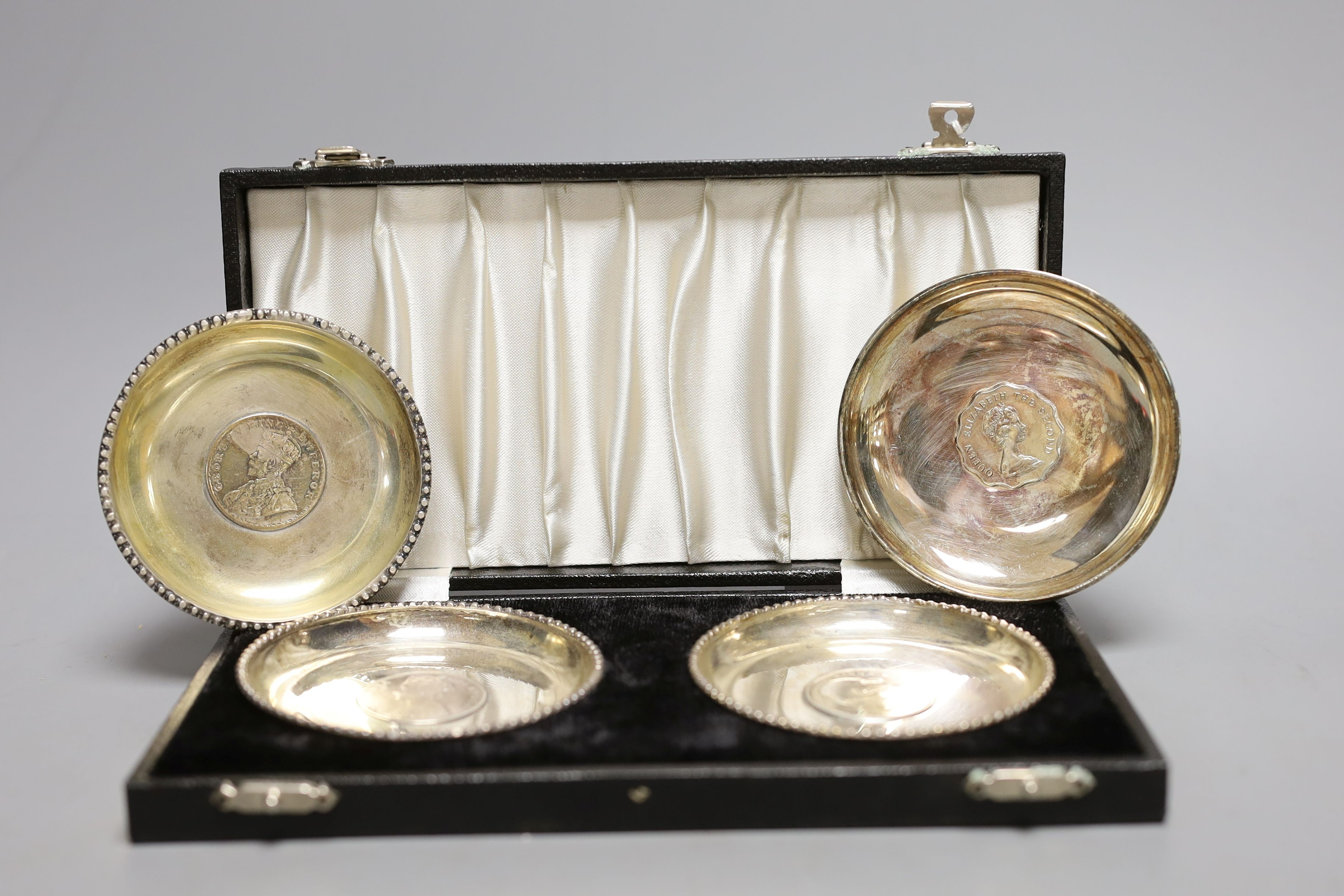 A cased pair of white metal inset coin small dishes and three other similar dishes.